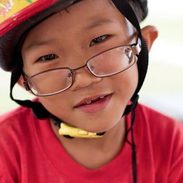 A young boy with glasses and a bike helmet on.