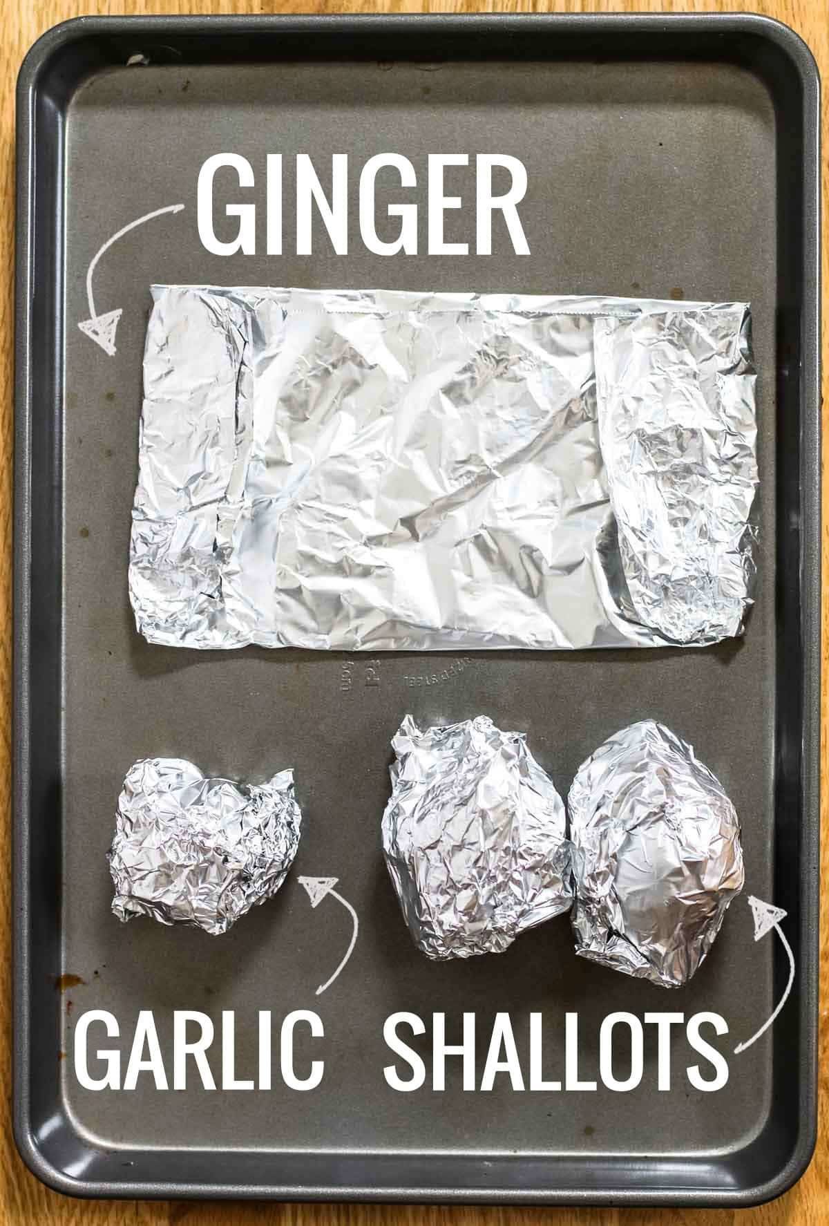 Ginger, garlic, and shallots wrapped in foil on a sheet pan.