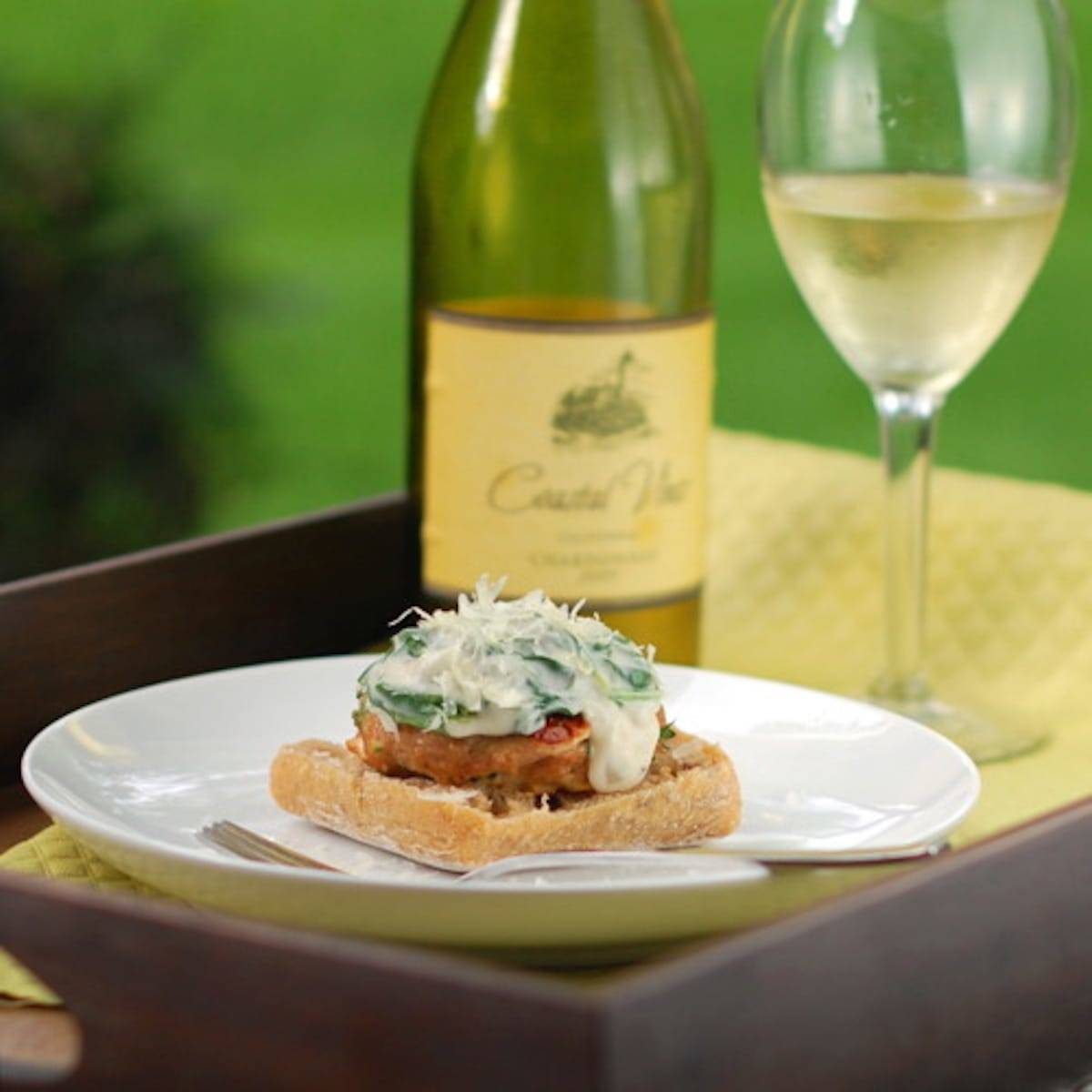 Garlic Parmesan Burger with Creamed Spinach Sauce on a white plate with a glass of wine.