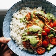 Salmon in a bowl with tomato salad, rice, and basil sauce.
