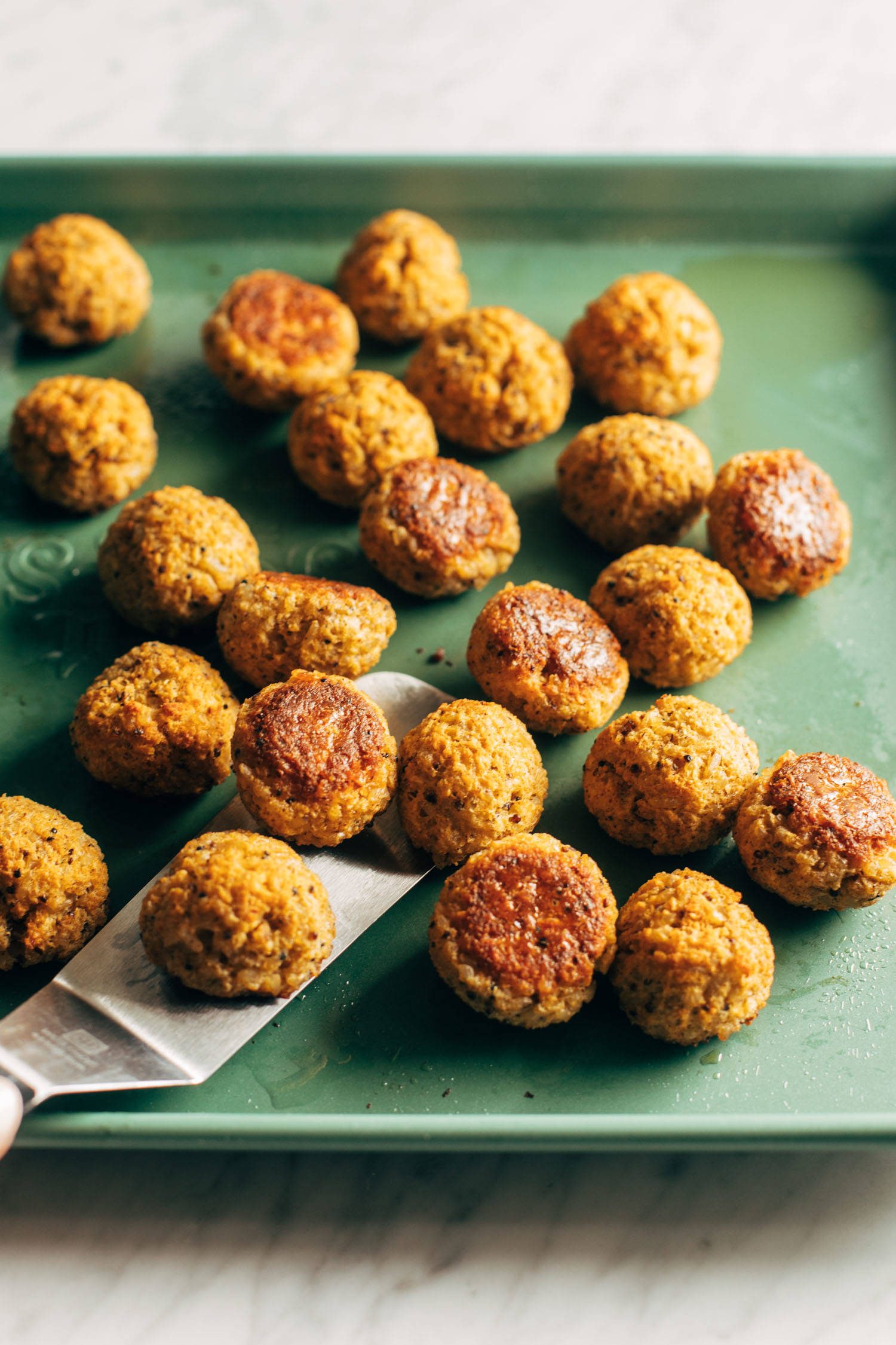 Cauliflower vegetarian meatballs on a sheet pan being scooped up with a spatula.