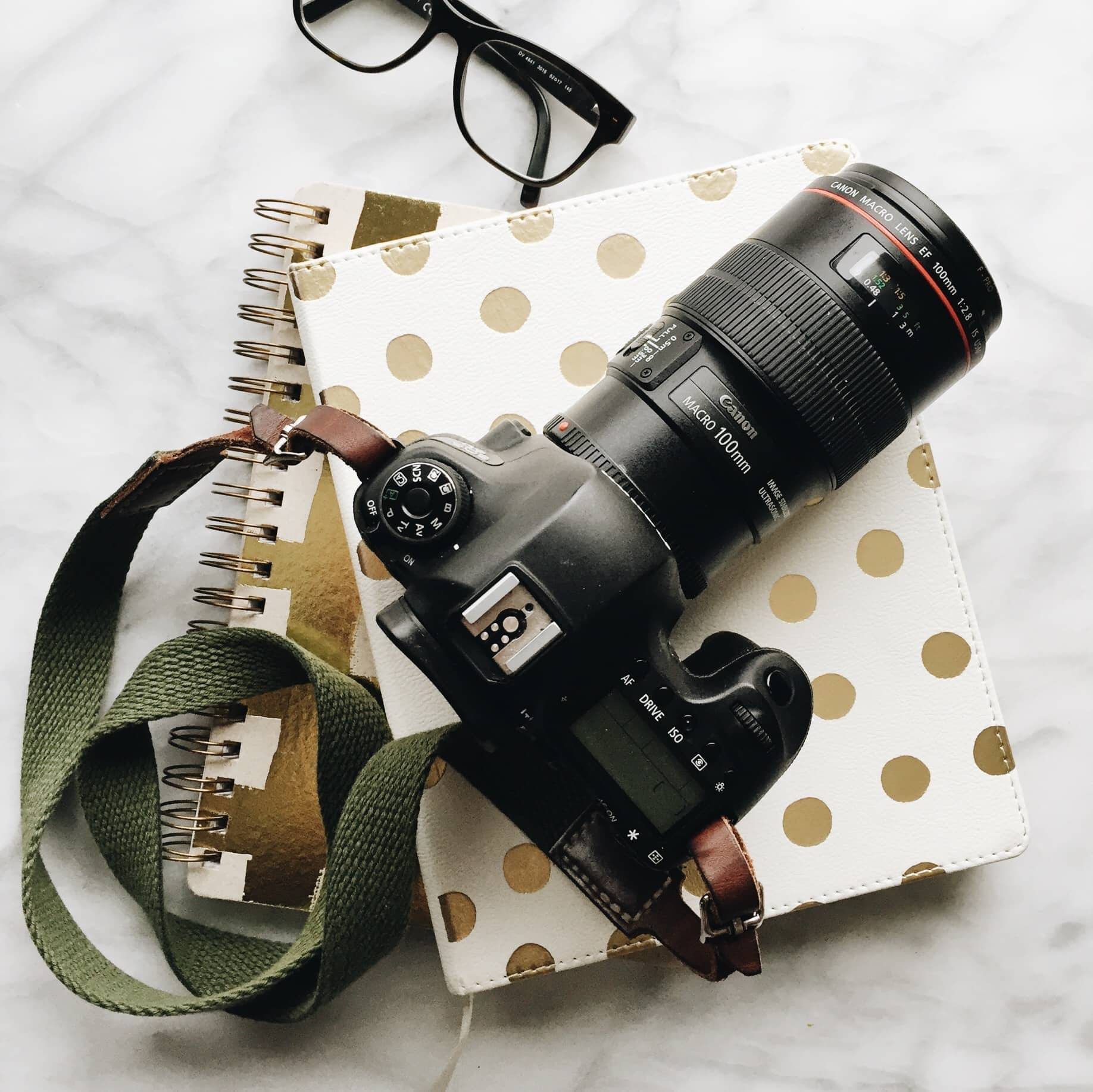camera with green strap on two notebooks with glasses