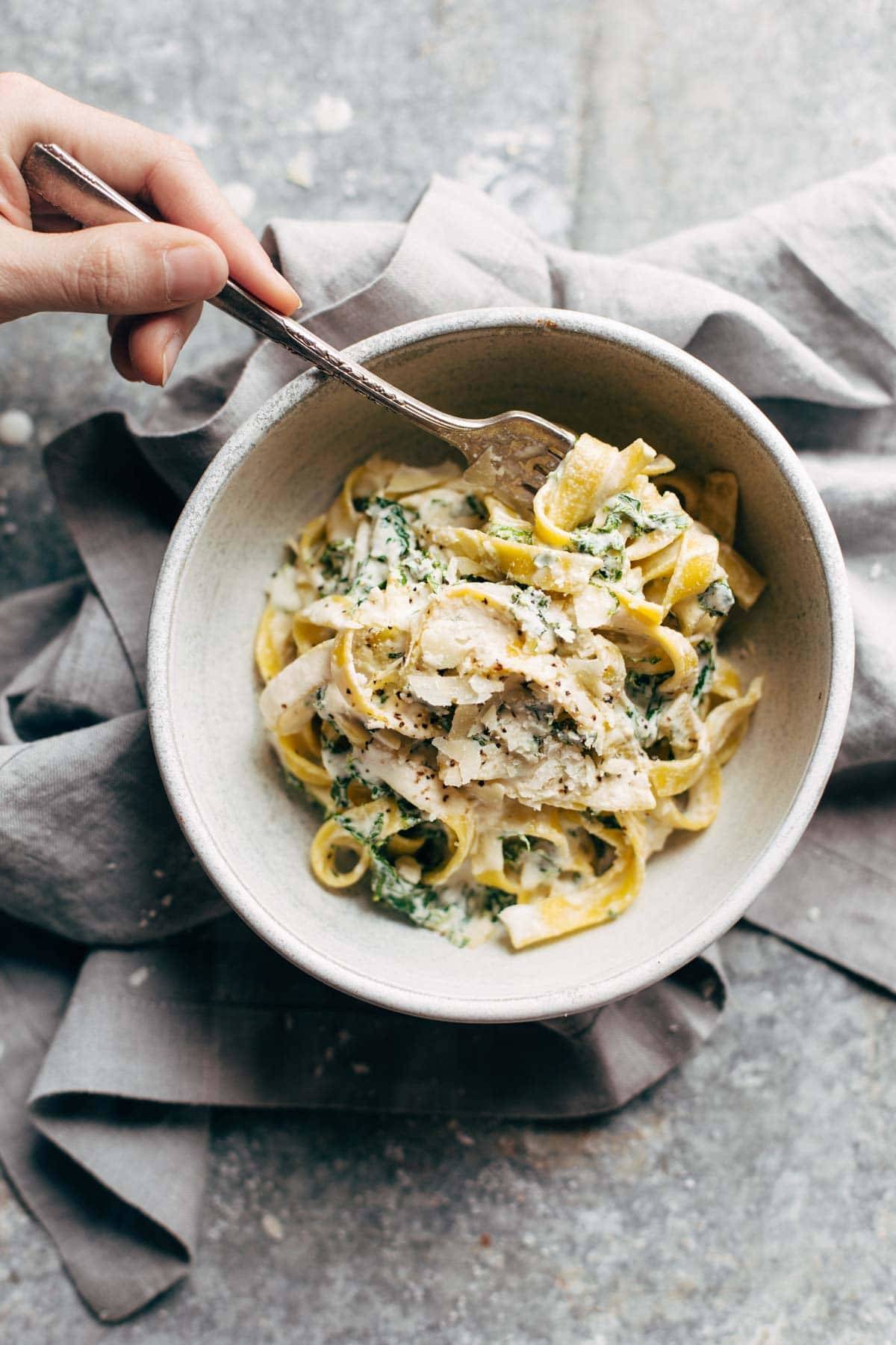 Kale pasta in a bowl with a hand holding a fork.