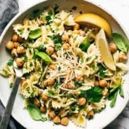 Pasta tossed with greens and cheese with lemon wedges.