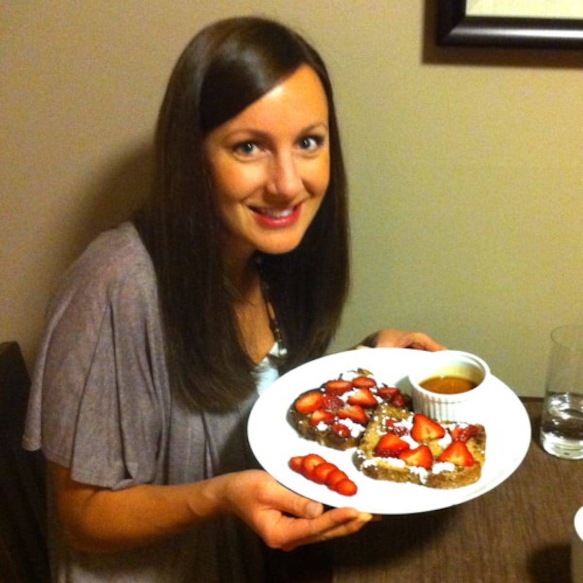 Woman holding a plate of stuffed french toast with strawberries, bananas, and maple syrup.